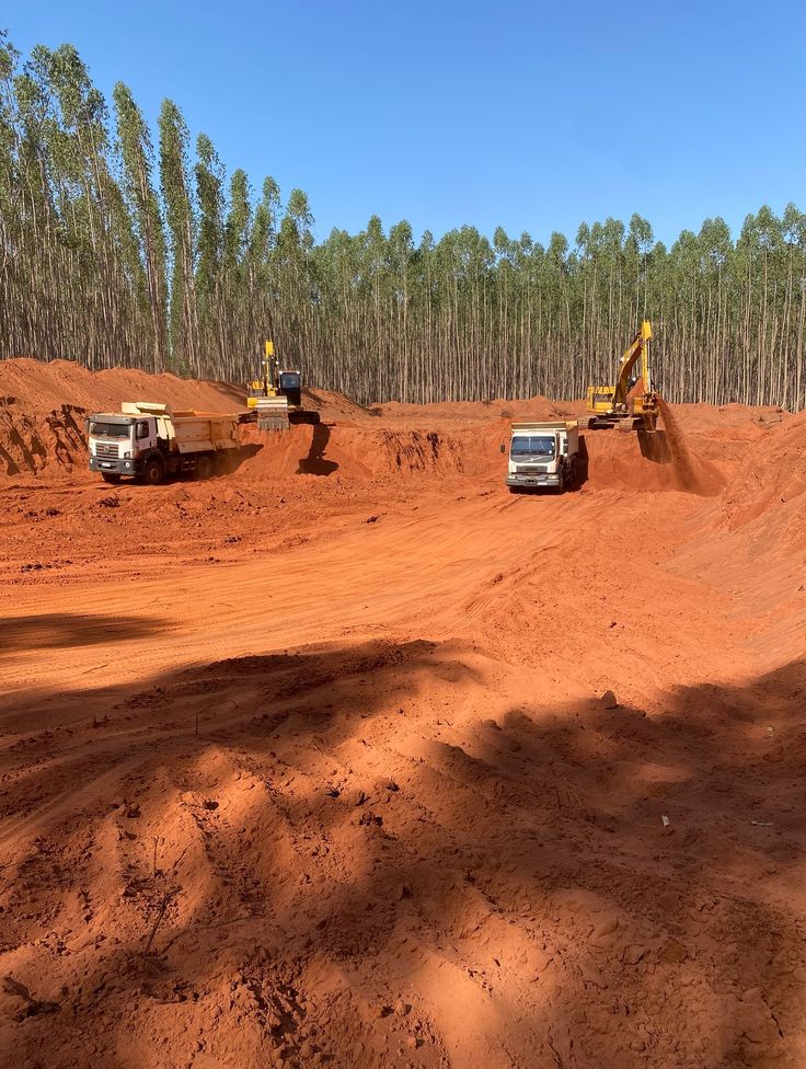 Escavadeiras e caminhões movimentando terra vermelha